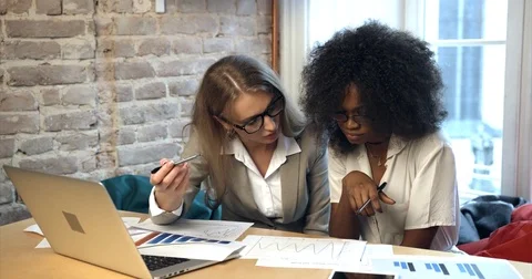 Close-up view of two young beautiful businesswomen working with graphics and Stock Footage 83363162