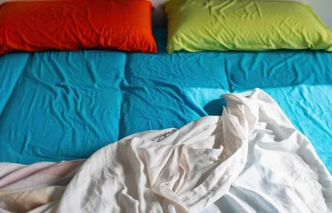 Close view of an unmade bed with bright turquoise sheets, an orange and lim.. Stock Photos