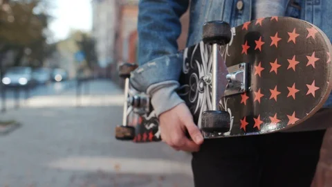 Close up view of unrecognizable man in jeans jacket holding the black skateboard Stock Footage 105257626