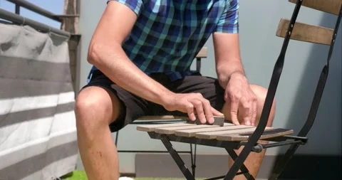 Close-up view of an unrecognizable man sanding a chair on the terrace of his Stock Footage 154636600