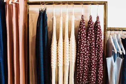 Close-up view of various stylish clothes hanging on hangers in boutique. Clothes Stock Photos