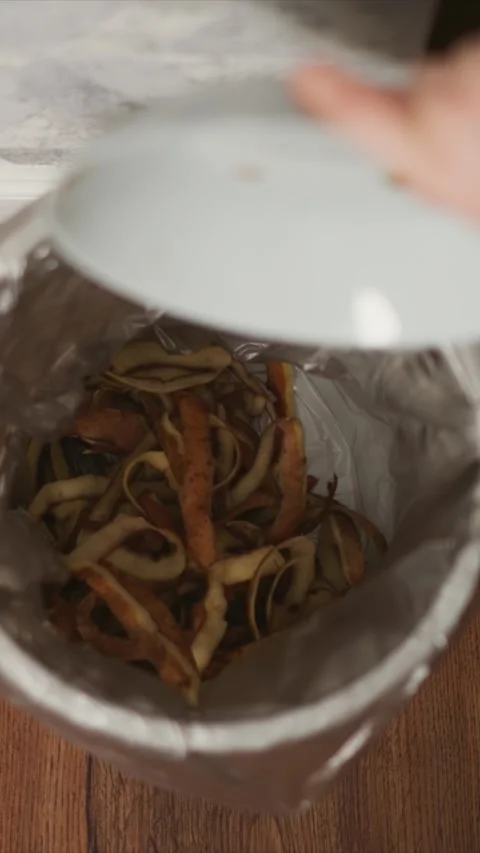 Close up view of vegetable peelings being poured into metal garbage bin with Stock Footage 345980380