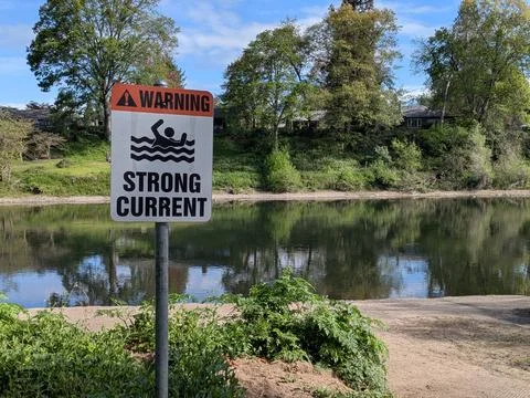 Close view of warning sign for strong river current with flowing Fotos Stock