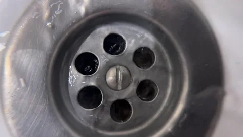 Close up view of water draining down a shiny clogged metal sink drain Stock Footage 320743088