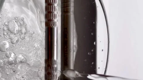 A close view of water flowing from a shiny metallic object in a glass container Stockbeeldmateriaal 283377125