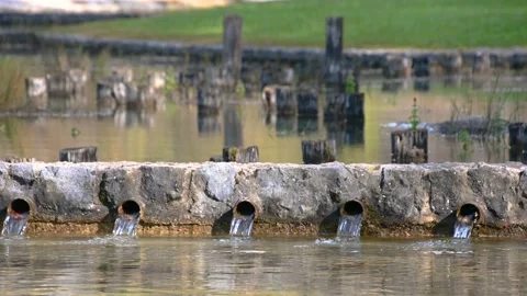 Close up view water flows thru iron pipes in small shallow pond Stock Footage 143433298