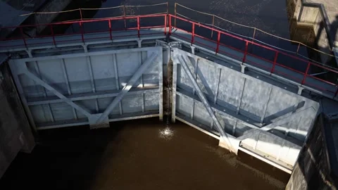 A close-up view of a water lock gate with red railings, holding back brownish wa Stock Footage 309332400