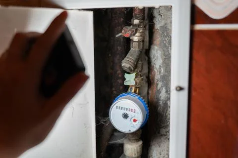 A close-up view of a water meter installed on an old plumbing pipe inside a Stock Photos