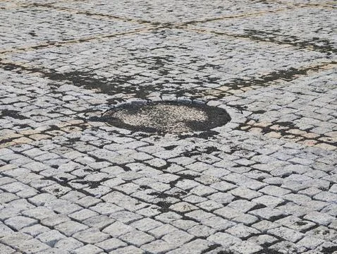 Close up view of weathered cobblestone pavement with circular pothole, dark.. Stock Photos