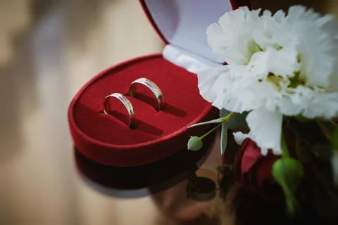Close up view of wedding rings in a red velvet box and white flowers on a gla Stock Photos