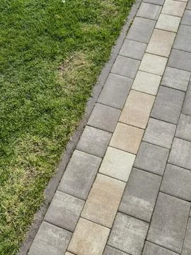 Close-up view of a well-maintained brick path alongside a patch of green grass Stock Photos