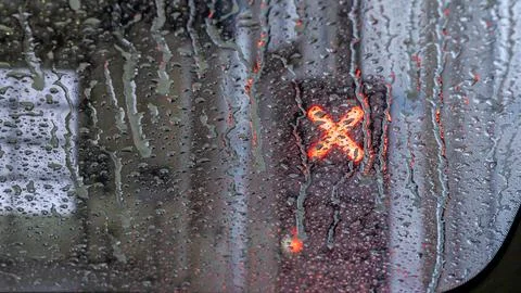 Close-up view of a wet car window with raindrops and a red illuminated cross Foto stock