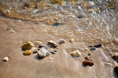 Close-up view of wet pebbles and sand on the shoreline with gentle waves Stock Photos