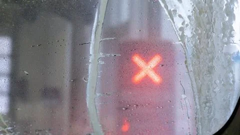 Close-up view of a wet window with raindrops and a blurred red cross signal in Stock Photos