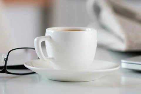Close up view of white coffee cup on table with glasses and newspaper Stock Photos