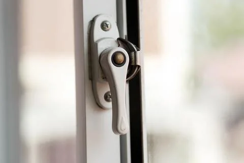 Close-up view of a white metal window handle latch mechanism installed on a.. Stock Photos