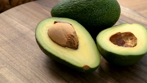 Close-up view of a whole and half avocado rotating on a wooden plate Stock Footage 272224887