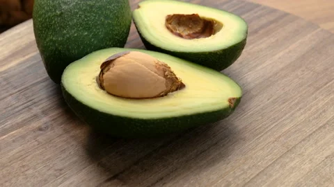 Close-up view of a whole and half avocado rotating on a wooden surface Stock Footage 272224916