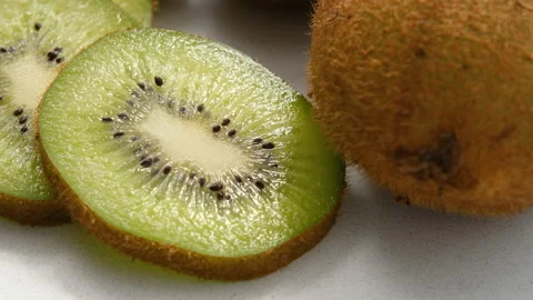 Close-up view of whole and sliced kiwi rotating counterclockwise on a marble Stock Footage 272257912