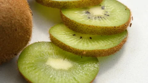 Close-up view of whole and sliced kiwi rotating on a marble surface Stock Footage 272257934