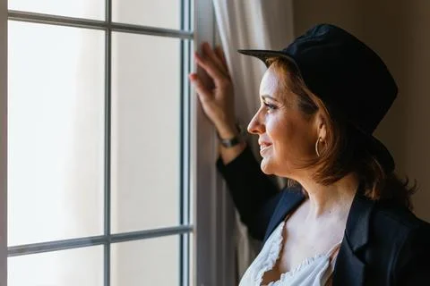 Close-up view of a woman while looking out window standing at home. Stock Photos