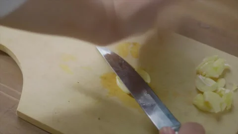 Close-up view of woman's hands with a knife crush the garlic on a chopping .. Stock Footage 329703402
