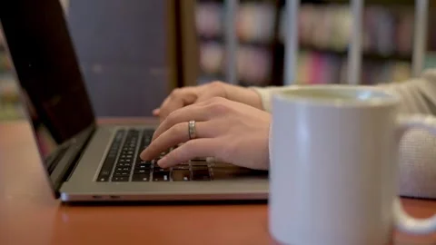 Close view of a woman's hands typing on a laptop keyboard with a coffee mug i Stockbeeldmateriaal 275799190