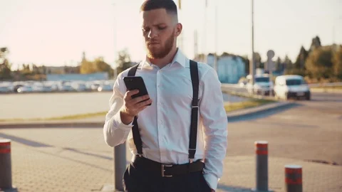 Close up view of young bearded man walking down street focused on using phone at Stock Footage 115668711