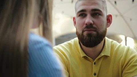 Close-up view of young bearded man in yellow polo sitting in outdoor cafe with 動画素材 139973537