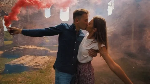 Close view of a young beautiful couple kissing holding smoke bombs in their Vidéo 124641424