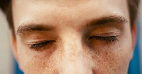 Close-up view of the young guy with freckles opening his green eyes and looking Stock Footage 92011944