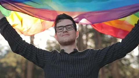Close up view of young handsome man in glasses smiling, posing with rainbow flag Stock Footage 137325468