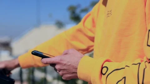 Close-up view of young man hand using smartphone outside riding scooter enjoying 스톡 동영상 211727216