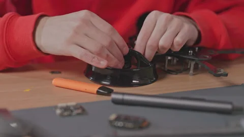 Close-up view of young man in red hoodie fixing details of quadcopter. Shot of Stock Footage 186156750