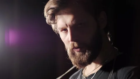 Close up view of a young strong man with a beard sits on a tire in a dark gym. Stock Footage 142229720