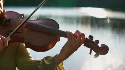 Close-up of a violinist playing soothing classical music outdoors by a tranquil Stock Footage 340217848