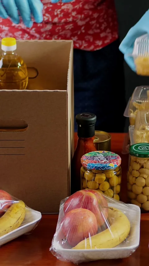 Close-up, Volunteers in protective gloves pack grocery to cardboard Donation Stock Footage 320347017