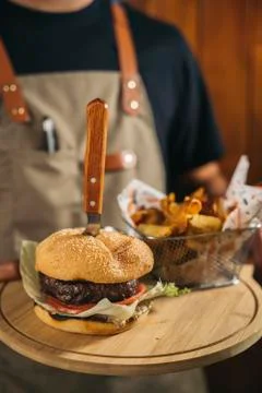 Close-up of a waiter using face mask serving a delicious meat burger with fries Stock Photos