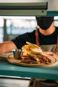 Close-up of a waiter using face mask serving a delicious meat dish with fries Stock Photos
