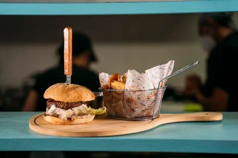 Close-up of a waiter using face mask serving a delicious meat burger with fries Stock Photos