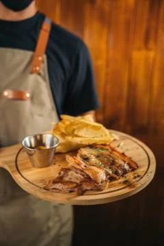 Close-up of a waiter using face mask serving a delicious meat dish with fries Stock Photos