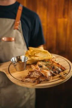 Close-up of a waiter using face mask serving a delicious meat dish with fries Stock Photos