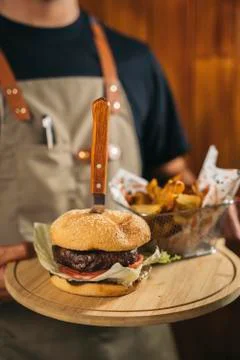 Close-up of a waiter using face mask serving a delicious meat burger with fries Foto stock