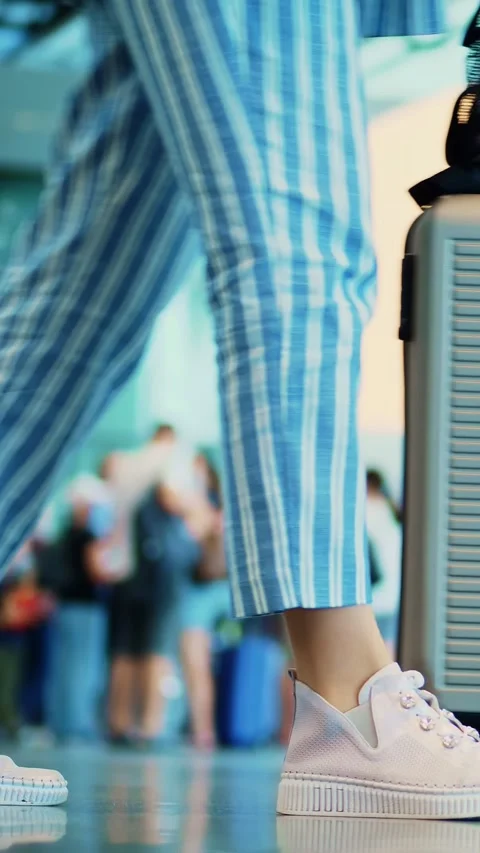 Close-up of walking legs in sneakers, with suitcase on wheels, through airport Stock Footage 320957959