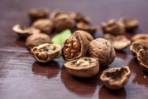 Close up of walnuts in shell and some broken on brown colored wooden surface. Stock Photos
