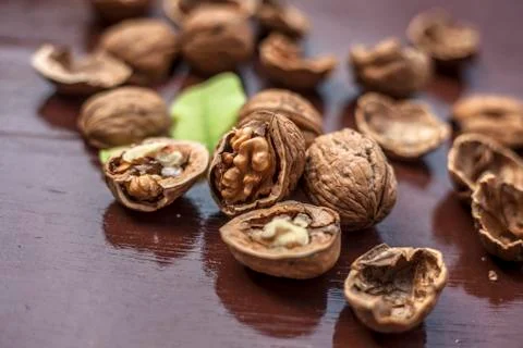 Close up of walnuts in shell and some broken on brown colored wooden surface. Stock Photos