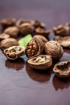 Close up of walnuts in shell and some broken on brown colored wooden surface. Stock Photos