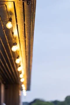 Close-up of warm glowing string lights hanging from a wooden roof at dusk Foto stock