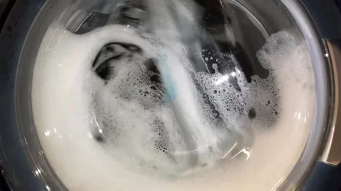 Close-up of a washing machine door. The drum spins the blue and white linen Stock Footage 150312641