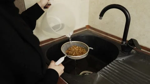 Close-up of water being poured over golden raisins in a metal sieve above a.. 動画素材 332159836